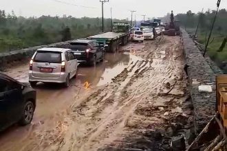 Kendaraan berusaha melewati satu titik ruas jalan yang rusak.