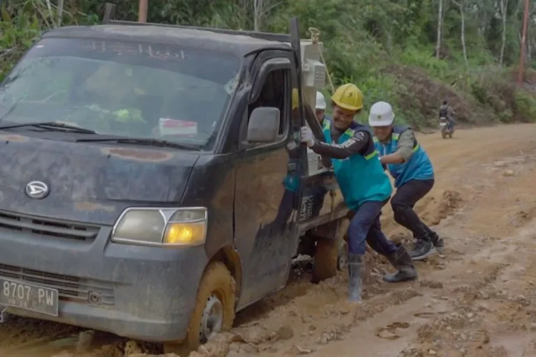 Petugas PLN tengah mendorong mobil yang terjebak lumpur saat berupaya wujudkan pembangunan infrastruktur listrik desa.