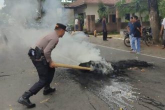 Petugas kepolisian saat memadamkan ban bekas dan membuka blokir jalan raya depan Kantor Desa Ketara. Sumber foto : RadarLombok