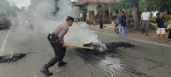 Petugas kepolisian saat memadamkan ban bekas dan membuka blokir jalan raya depan Kantor Desa Ketara. Sumber foto : RadarLombok